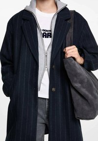 Marinblårandig ullblandad kappa med veckade slag, framknäppning, kombinerad med en grå zip-up sweatshirt med krage och en grå mocka axelväska.