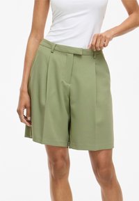 Pantalones cortos plisados verdes con pierna ancha, hechos de una tela suave. Presentan una cintura con pasador y bolsillos laterales.