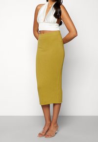 Halenkový bílý top spárovaný s šitým hořčicově žlutým úpletem do délky kolen. Tkanina má hladkou texturu a minimální švy.