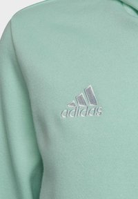 Zielona bluza z miękką fakturą, z srebrnym, haftowanym logo Adidas po lewej stronie. Klasyczny fason z kapturem.