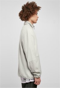 Lysegrå zip-up genser laget av teksturert fleece, med ståkrage, lange ermer, og en framlomme med en glatt stoffdetalj.