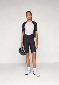 Juoda dviračių apranga, įskaitant trumpomis rankovėmis marškinėlį, šortus su petnešomis ir tekstūruotą pagrindinį sluoksnį. Priedai: juoda šalmą ir balti dviračių batai.