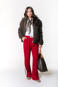 Brun fleecejacka, vit topp, röda byxor med sidostenar, scarf i leopardmönster, brun väska och beige skor. En enkel bakgrund.