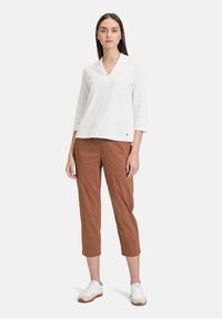 Top bianco con scollatura a V e maniche a 3/4, abbinato a pantaloni marroni a pantalone cropped. Le scarpe sono bianche con suola color sabbia. Design semplice, senza motivi o accenti.