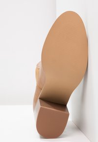 Botín de tobillo de cuero marrón claro con tacón cuadrado. Acabado suave, suela texturizada con estrías y forma de punta redonda. La base es de goma marrón clara.