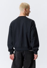 Black sweatshirt with a crew neckline, long sleeves, and ribbed hem. Made of smooth fabric, featuring a relaxed fit and minimal design.
