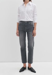 Jeans rectos de color gris oscuro, tela ligera, cintura alta, cinco bolsillos, combinados con una camisa blanca de botones y zapatos negros sin cordones.