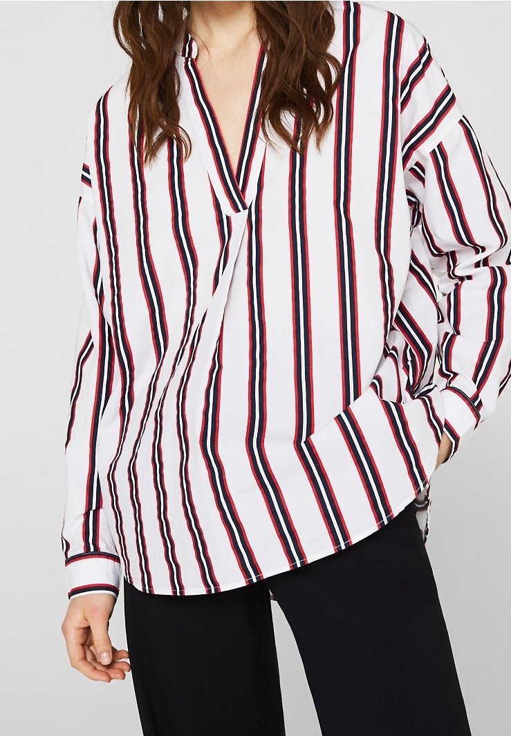 Blusa bianca a righe con strisce verticali rosse e blu, scollatura a V, maniche lunghe e vestibilità rilassata. Tessuto morbido con una texture liscia.