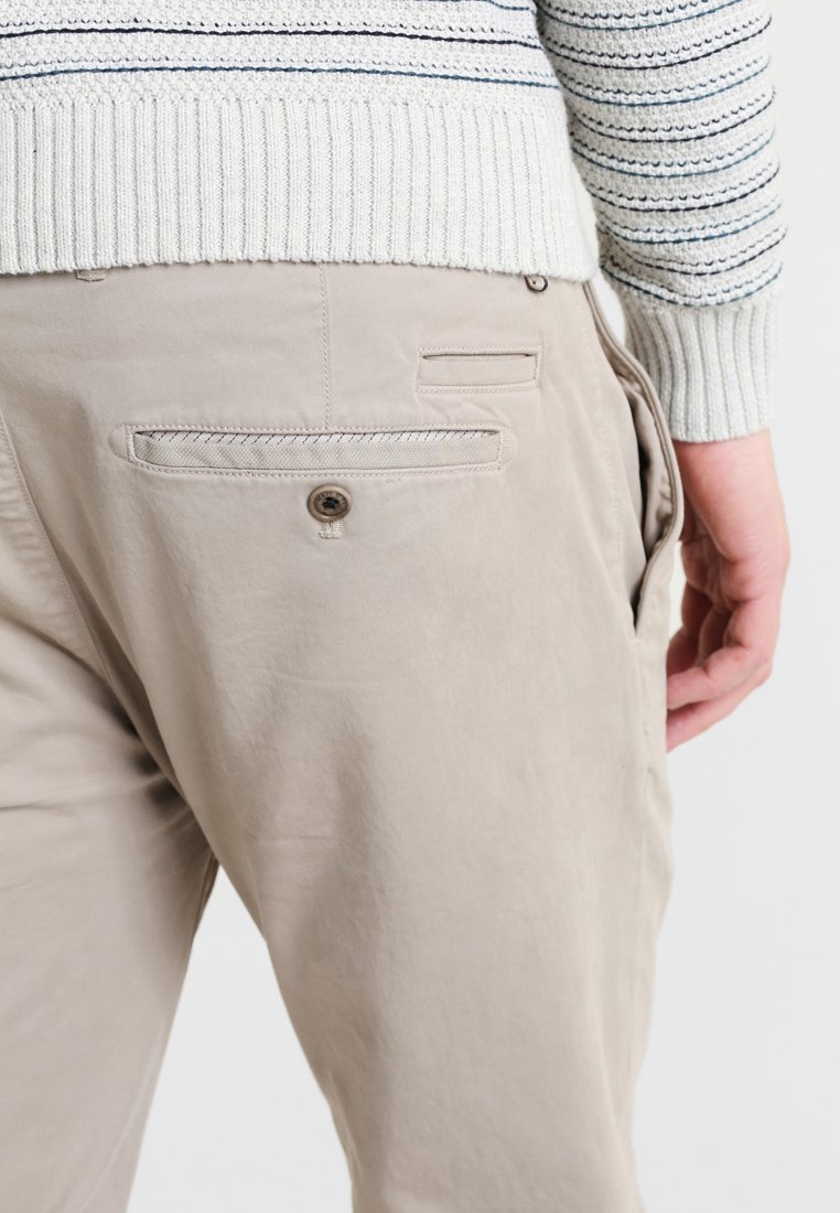 Helle beigefarbene Hosen mit glatter Textur, ausgestattet mit einer Gesäßtasche mit Knopfverschluss und einer zusätzlichen Eingrifftasche an der Seite.