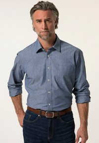 Camicia con bottoni in tessuto chambray azzurro chiaro, con taschino sul petto e maniche arrotolate. Abbinata a jeans in denim scuro e una cintura marrone.