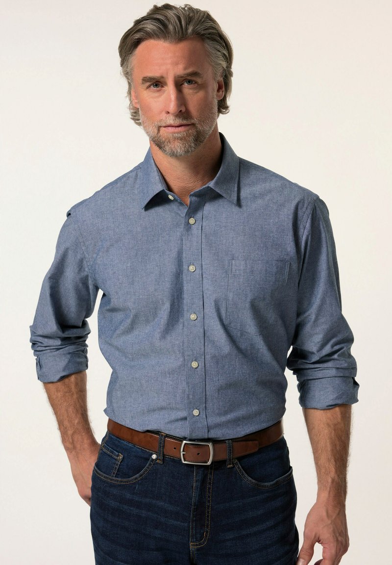 Camicia con bottoni in tessuto chambray azzurro chiaro, con taschino sul petto e maniche arrotolate. Abbinata a jeans in denim scuro e una cintura marrone.