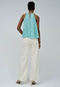 Haut halter plissé bleu clair avec un design texturé, associé à un pantalon large blanc. Détail notable d'une ouverture au dos et de quincaillerie dorée.