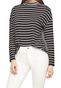 Mustat ja valkoiset raidoitetut pitkähihainen paita, jossa on korkea kaulus ja rento malli. Yhdistetty valkoisiin farkkuihin, jotka näyttävät pehmeältä ja sileältä kangasrakenteelta.