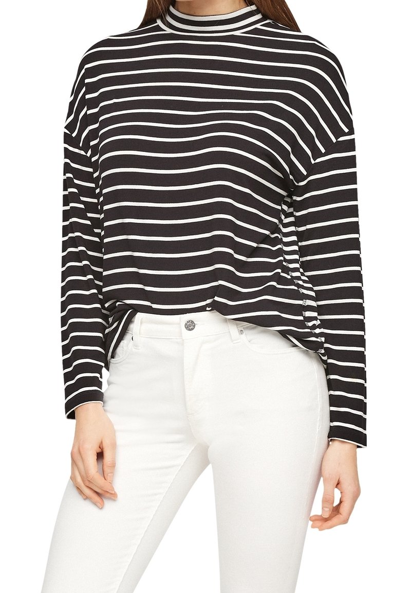 Mustat ja valkoiset raidoitetut pitkähihainen paita, jossa on korkea kaulus ja rento malli. Yhdistetty valkoisiin farkkuihin, jotka näyttävät pehmeältä ja sileältä kangasrakenteelta.