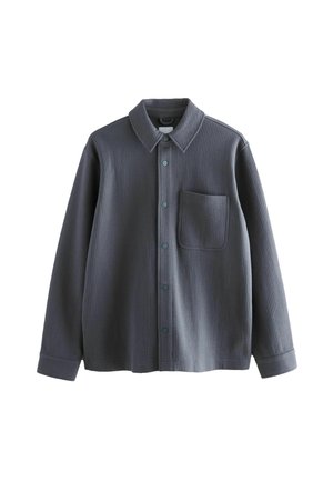 Szürke ing, bordás anyagból készült, galléros nyakkal, elülső zsebbel és kontrasztos gombokkal. Hosszú ujjak mandzsettával.