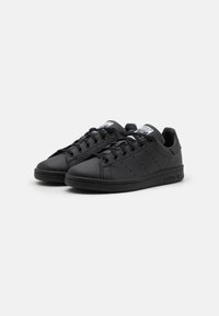 Sorte lædersneakers med en glat overflade, snørebåndsdesign, perforeringer på siderne og en flad sål. Har et mærketunge-label.