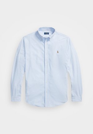 Chemise bleu clair à manches longues avec des rayures verticales blanches, ornée d'un petit logo brodé sur la poitrine et d'un col évasé.