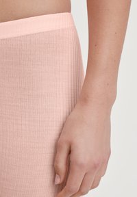 Close-up van een hand die naast een heup rust en roze geribbelde stofshorts draagt tegen een effen lichte achtergrond.