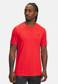 T-shirt sportivo rosso realizzato in tessuto traspirante, con maniche corte, colletto a giro e un piccolo logo nero sul petto.