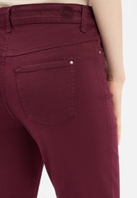 Burgunderfarbene Denim-Jeans mit einer figurbetonten Passform, mittelhoher Taille, Gesäßtaschen und dezenten Nähten. Weicher Stoff mit Stretch.