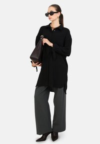 Zwarte langarmshirt met strikken bij de manchet, gecombineerd met brede grijze broeken en spitse bruine enkelboots. Bevat zonnebril en een bruine handtas.