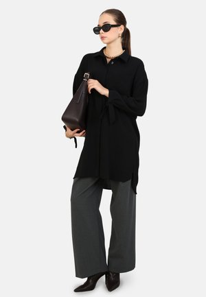Black long-sleeve shirt with ties at the cuffs, paired with wide gray trousers and pointed brown ankle boots. Features sunglasses and a brown handbag.