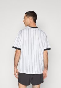 Hvidstripet kortærmet skjorte med sort krave og manchetter, der har en afslappet pasform. Stoffet virker glat med en let tekstur.