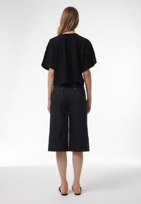 Top corto negro con mangas cortas, combinado con culottes negros de pierna ancha. Textura suave; diseño minimalista; solo vista desde atrás.