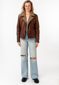 Bruine leren jack met een faux shearling kraag, een rits aan de voorkant en zijzakken. Gecombineerd met lichtblauwe gescheurde jeans en zwarte laarzen.