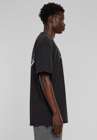 Svart oversized t-skjorte med korte ermer, med blå flammegrafikk på siden og en klassisk rund halslinning.