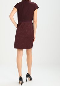 Burgundy dress with a smooth top and textured lower half, features short sleeves, knee-length cut, and black high-heeled shoes.