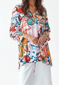 Tunique imprimée florale colorée en tissu léger. Caractérisée par un col en V, des manches trois-quarts et une coupe décontractée.