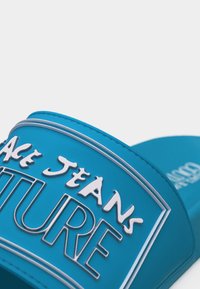 Μπλε σανδάλι με φαρδιά λουρί, με λευκό και ασημένιο ανάγλυφο κείμενο "PEACE JEANS FUTURE" στο λουρί.