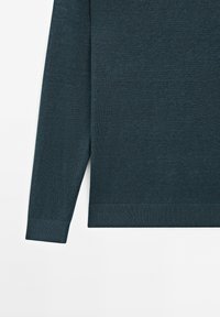 Ciemnoniebieski sweter z długim rękawem, dziany, z prążkowanymi mankietami i dołem, położony na białym tle.