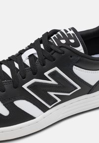 Baskets noir et blanc avec une tige en cuir, des lacets texturés, un logo bien visible et une semelle en caoutchouc contrastante.