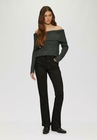 Dunkelgrauer Strickpullover mit schulterfreiem Design und gerippter Textur, kombiniert mit schwarzen schmal geschnittenen Hosen und Absatzstiefeln. Schlichtes und tailliertes Design.
