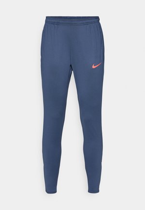 Tumed sinine spordipüksid kitseneva disainiga, elastne vöökoht ja väike oranž Nike logo vasakul reitel. Sile tekstuur.