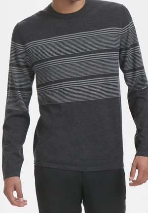 Man draagt een donkergrijze trui met lange mouwen met dunne lichtgrijze horizontale strepen over de borst en mouwen, gecombineerd met een zwarte broek.
