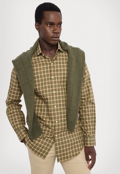 Green and beige plaid shirt with button closure, paired with a green sweater draped over shoulders, against a neutral background.