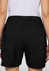 Svarta träningsshorts med elastisk midja och en lätt, slät textur. Har en perforerad design på toppen.