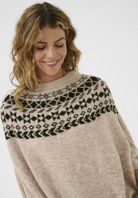 Gebreide pullover in lichtbeige wol met donkergroene geometrische patronen rond de halslijn. Zachte textuur en losse pasvorm, korte mouwen.