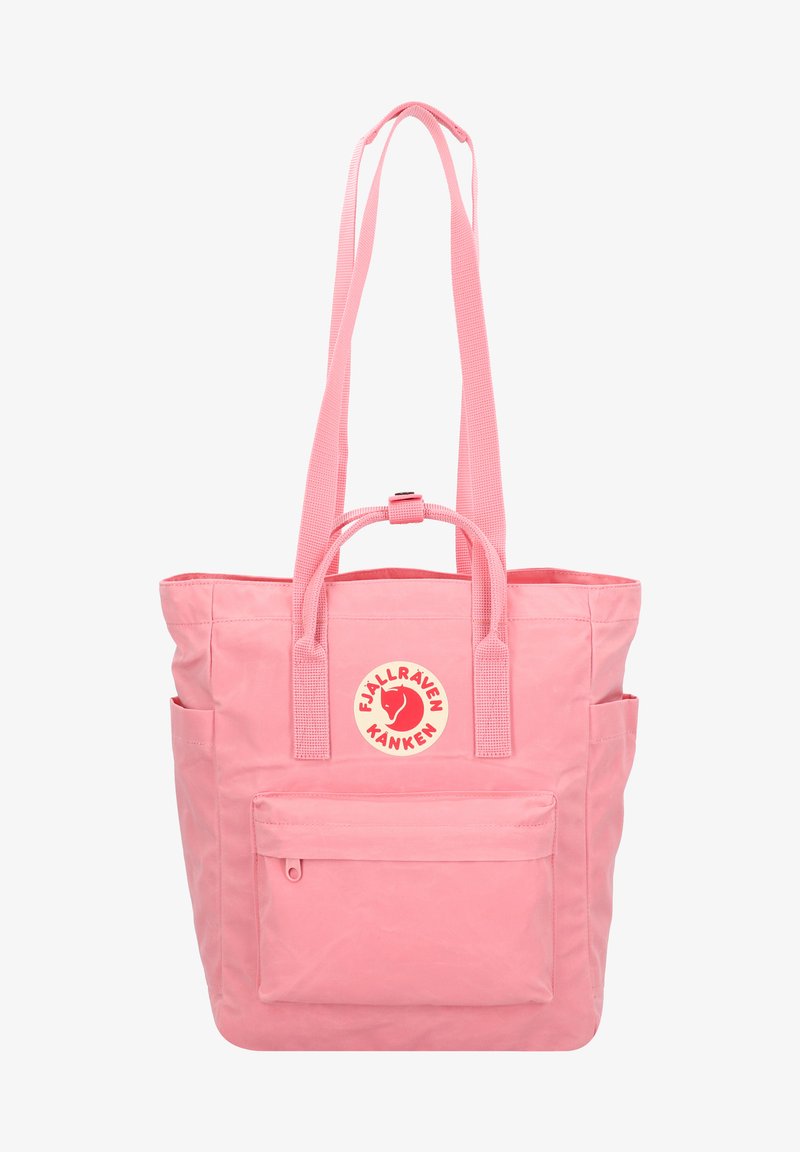 Vaaleanpunainen kangaskassi, joka on valmistettu kestävästä kankaasta. Kassi sisältää keskeisen logon tikkauksen, kaksi pitkää kahvaa ja etupuolella vetoketjullisen taskun. Rakenne on teksturoitu ja muotoilu on rento.