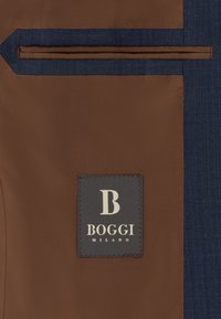 Intérieur de veste marron avec une petite poche et une étiquette en tissu gris cousue à l'intérieur indiquant BOGGI MILANO.