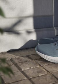 Pair of blue athletic running shoes resting on textured stone pavement beside a sunlit wall with shadows.