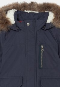 Granatowa ocieplana parka z kapturem wykończonym sztucznym futrem, zamek błyskawiczny z przodu, kieszenie boczne i wewnętrzna podszewka przypominająca polar.