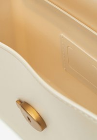 Interno della borsa color crema con superficie liscia e lucentezza delicata; presenta un dettaglio in hardware dorato e uno slot rettangolare per carte.
