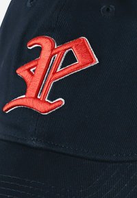 Granatowa czapka z czerwonym, haftowanym logo „AP”. Wykonana z teksturowanej tkaniny, z przeszyciami na górze. Posiada oczka wentylacyjne.