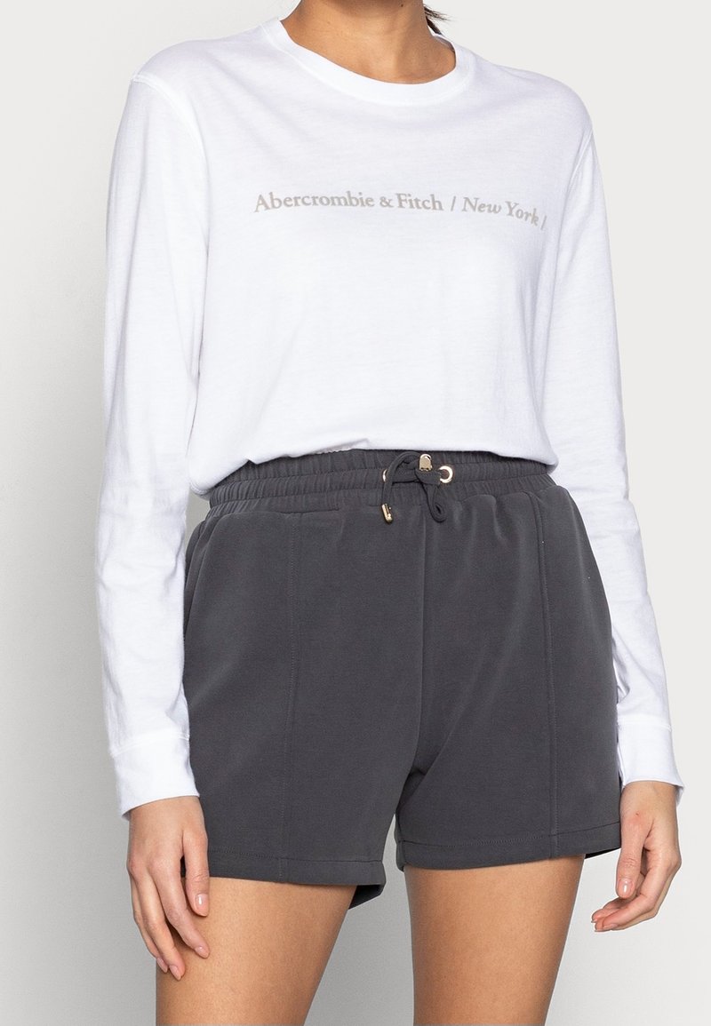 Witte langslurfshirt met "Abercrombie & Fitch / New York" in het grijs gedrukt. Gepaard met donkergrijze shorts met elastische tailleband en een trekkoord.