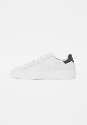Sneaker en cuir blanc avec une surface texturée et un bout rond. Présente un accent au talon bleu marine et cinq trous pour les lacets. Branding sur le côté.