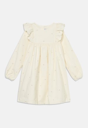 Langärmliges cremefarbenes Kleid mit Rüschenschultern, das mit kleinen Sternstickereien verziert ist. Baumwollstoff mit gerafftem Bund für mehr Volumen.
